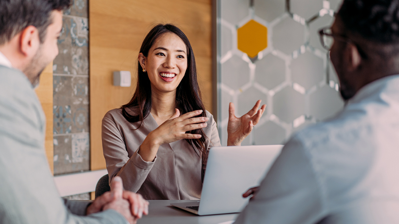 Image of a woman smiling sitting at a table with a laptop in front of her
