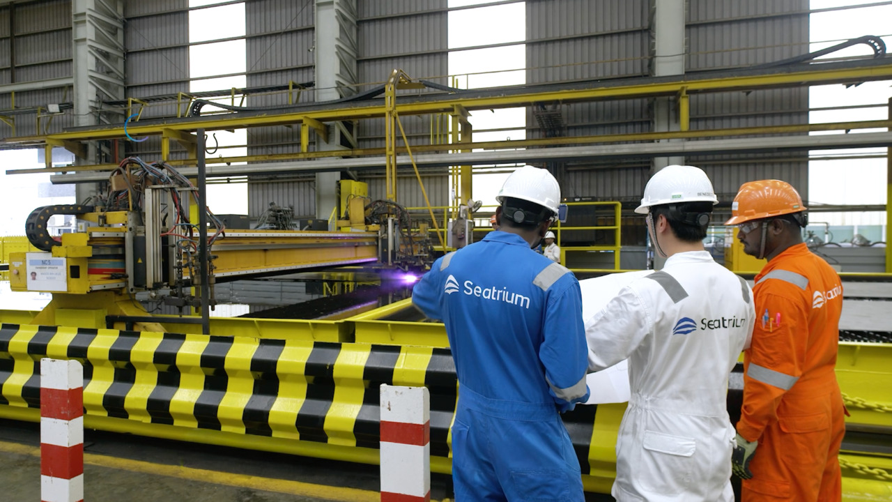 Image of three people in Seatrium jumpsuits, wearing hardhats