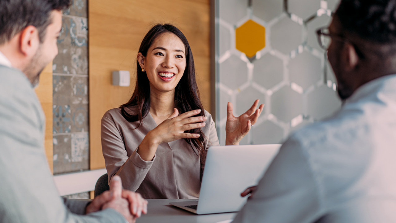 Image of a woman smiling sitting at a table with a laptop in front of her