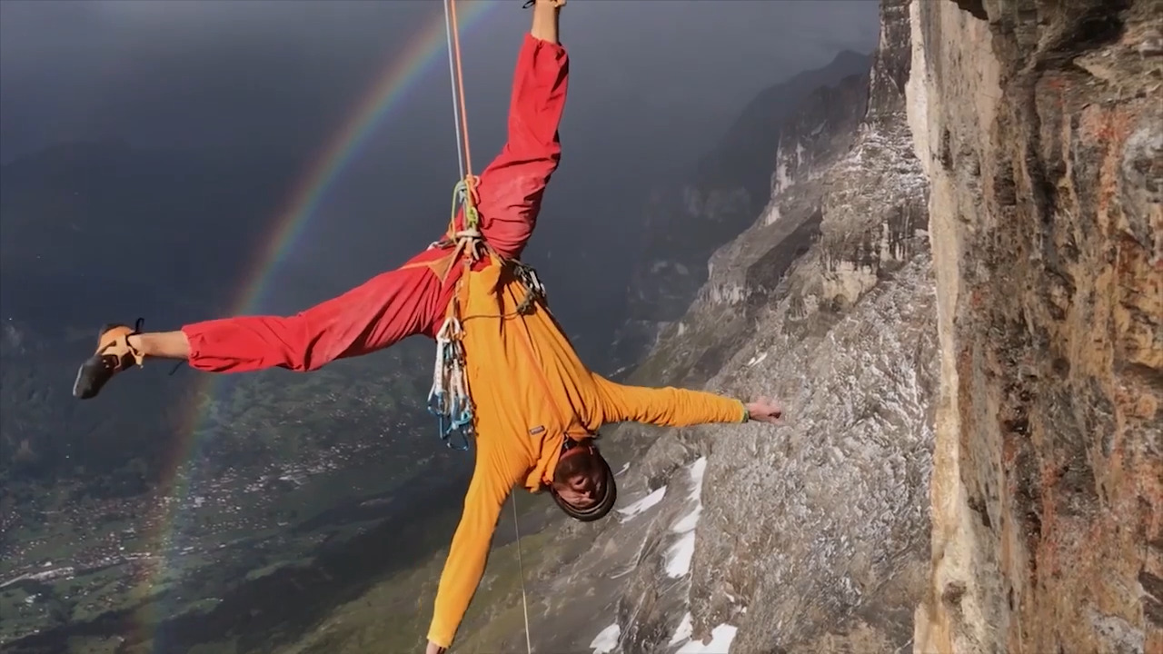 Image of a rock climber with a rainbow beyond them
