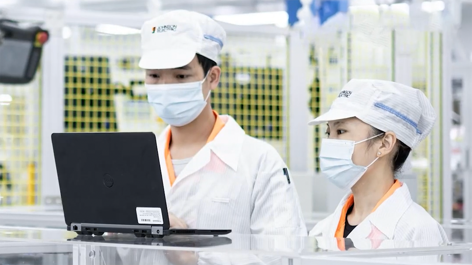 Image of a man and woman wearing masks, looking at a laptop in a factory